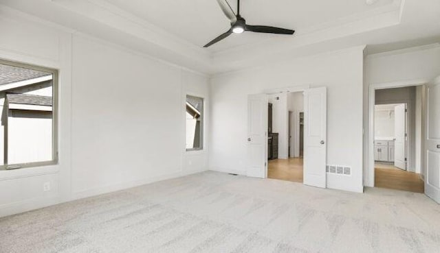 unfurnished bedroom with a raised ceiling, light colored carpet, and ceiling fan