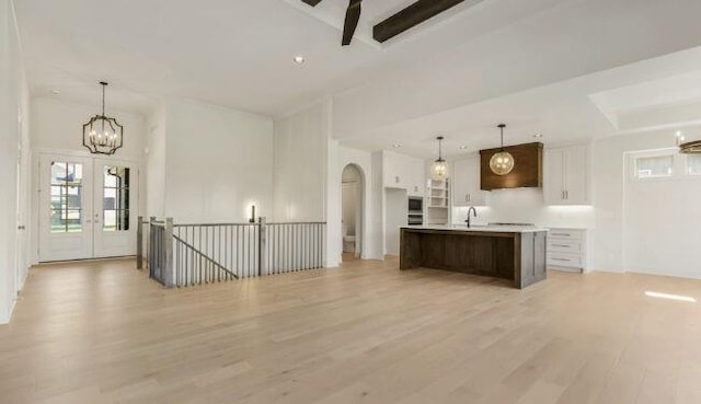 kitchen with hanging light fixtures, a kitchen island with sink, sink, and white cabinets