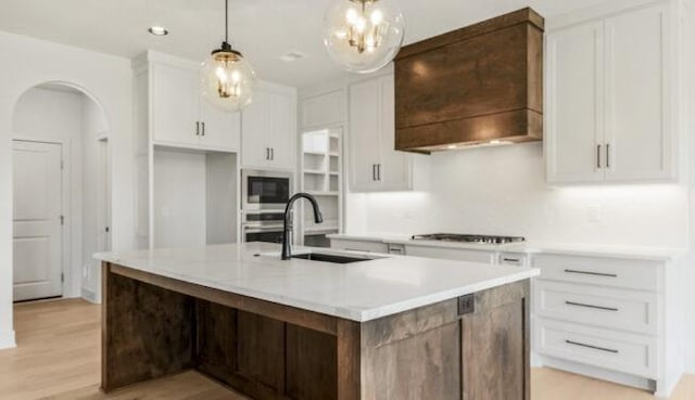 kitchen with pendant lighting, stainless steel appliances, a center island with sink, and white cabinets