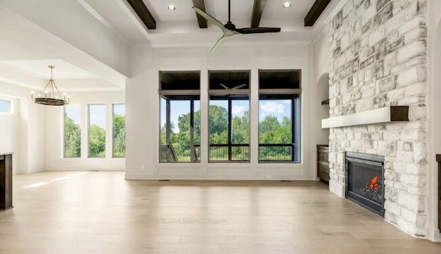 unfurnished living room with ceiling fan with notable chandelier, beam ceiling, a fireplace, and wood finished floors