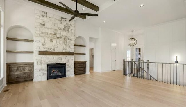 unfurnished living room with a stone fireplace, ceiling fan with notable chandelier, a high ceiling, wood finished floors, and beam ceiling