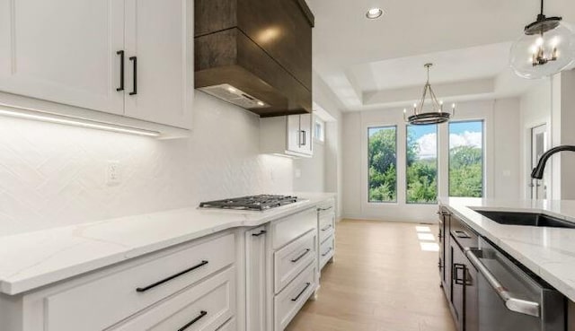 kitchen featuring a raised ceiling, light stone counters, stainless steel appliances, premium range hood, and a sink