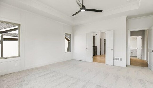 unfurnished bedroom with a raised ceiling, multiple windows, crown molding, and visible vents