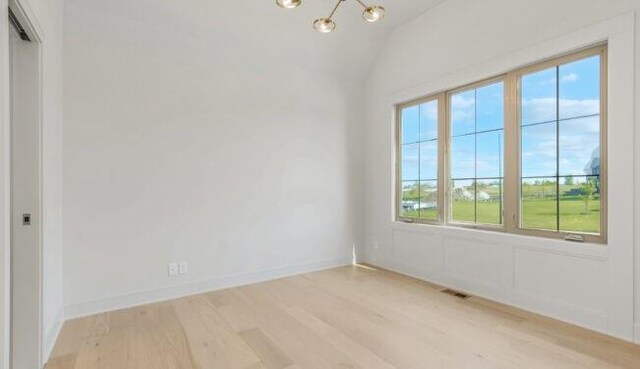 unfurnished room featuring lofted ceiling, light wood-style floors, baseboards, and a chandelier