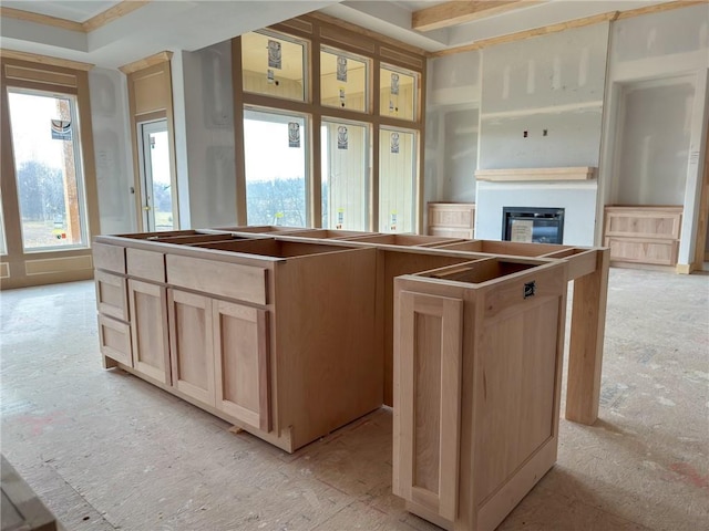 kitchen with light brown cabinets, a kitchen island, and a glass covered fireplace