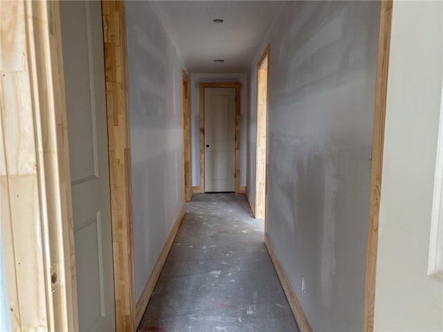 hallway with baseboards and unfinished concrete floors