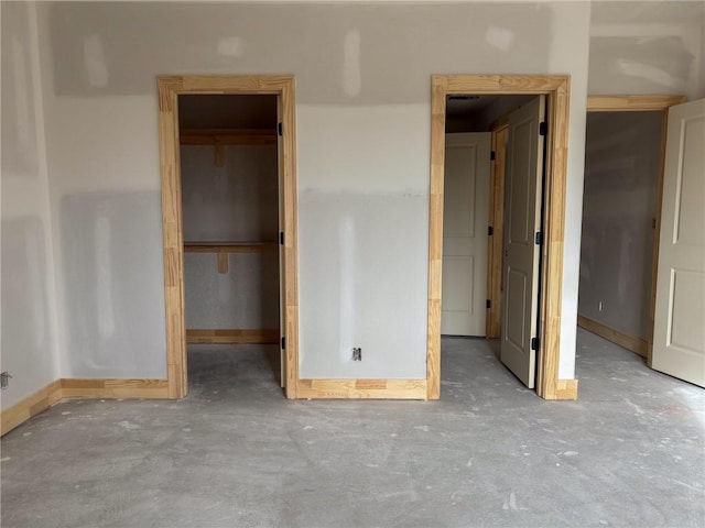 unfurnished bedroom with baseboards, a spacious closet, a closet, and unfinished concrete floors