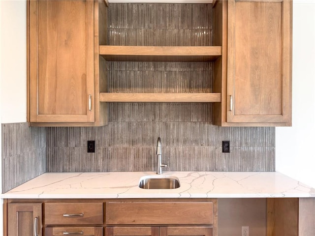 kitchen with open shelves, light stone counters, decorative backsplash, and a sink
