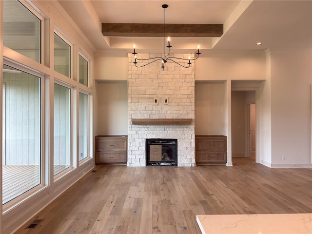unfurnished living room with a stone fireplace, visible vents, beamed ceiling, a chandelier, and hardwood / wood-style floors