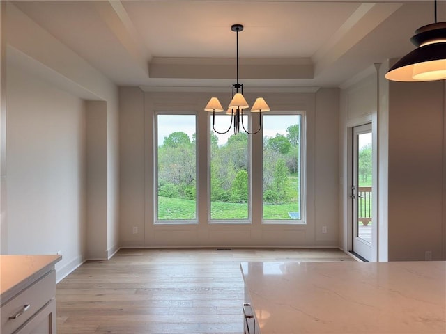 unfurnished dining area featuring light wood-type flooring, a raised ceiling, baseboards, and a notable chandelier