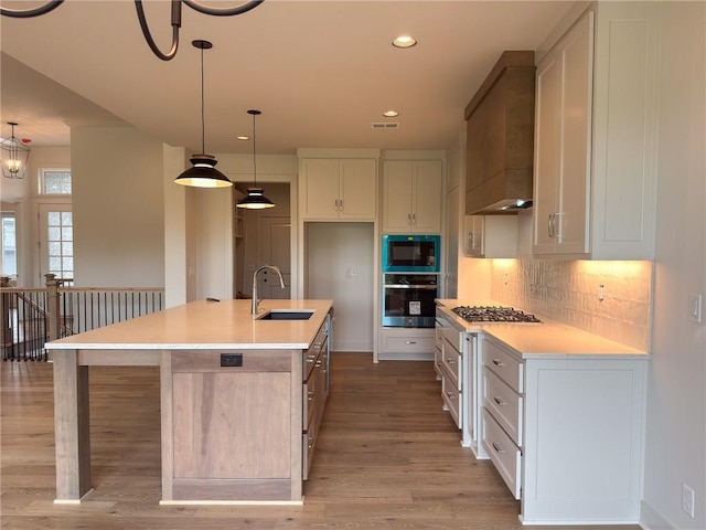 kitchen featuring premium range hood, tasteful backsplash, a sink, light wood-style flooring, and appliances with stainless steel finishes