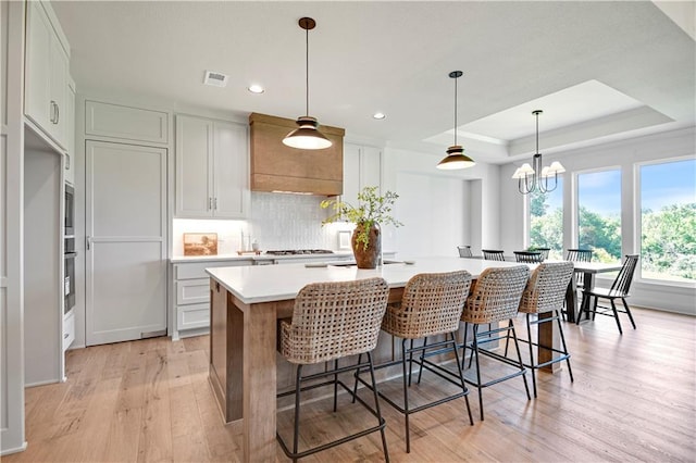22063 W 100th Ter, Lenexa, KS 66220 - kitchen featuring light wood-type flooring, light countertops, decorative backsplash, an island with sink, and a tray ceiling