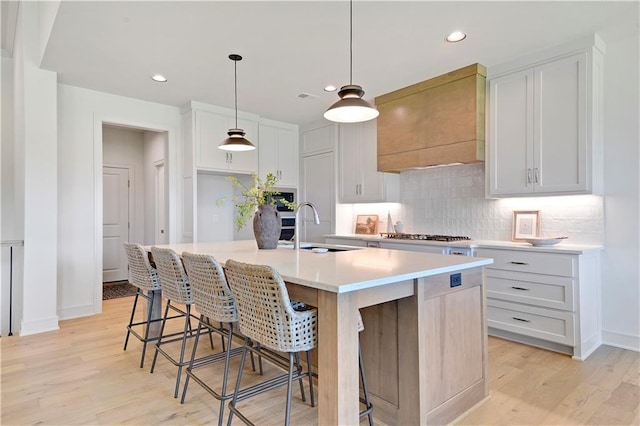 22063 W 100th Ter, Lenexa, KS 66220 - kitchen featuring decorative backsplash, a center island with sink, light wood-type flooring, white cabinetry, and light countertops