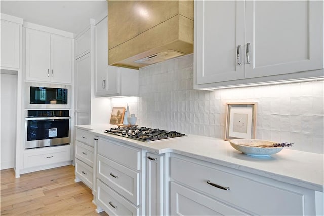 22063 W 100th Ter, Lenexa, KS 66220 - kitchen with appliances with stainless steel finishes, custom range hood, tasteful backsplash, white cabinetry, and light wood finished floors