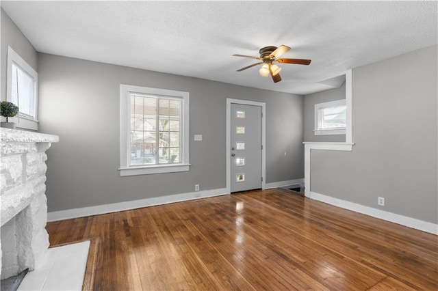 unfurnished living room with a fireplace, ceiling fan, wood-type flooring, and a textured ceiling