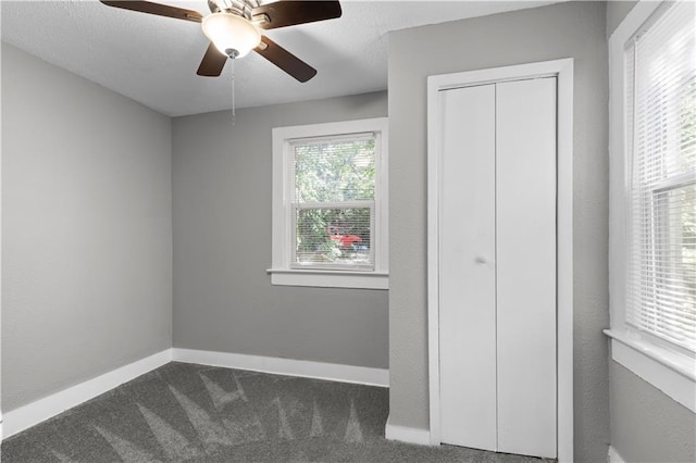 unfurnished bedroom featuring ceiling fan, a textured ceiling, a closet, and dark carpet