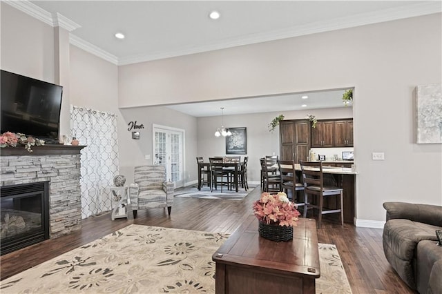 living room with a stone fireplace, a notable chandelier, dark hardwood / wood-style floors, and ornamental molding