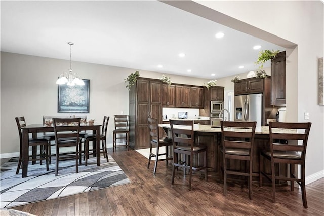 kitchen with decorative light fixtures, a kitchen island with sink, appliances with stainless steel finishes, dark hardwood / wood-style floors, and an inviting chandelier