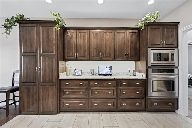 kitchen featuring dark brown cabinetry, appliances with stainless steel finishes, and light stone counters