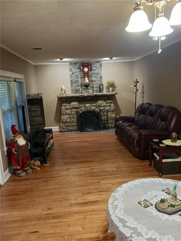 living room with a stone fireplace, crown molding, and hardwood / wood-style floors