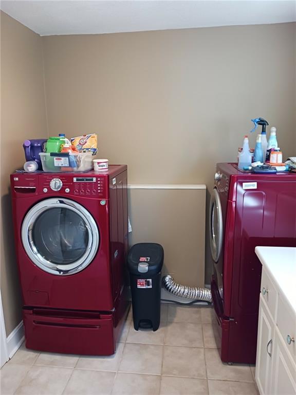 washroom with washing machine and dryer, light tile patterned floors, and cabinets