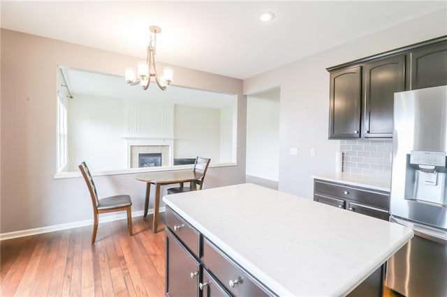 kitchen featuring a tiled fireplace, tasteful backsplash, hanging light fixtures, stainless steel fridge, and dark hardwood / wood-style flooring