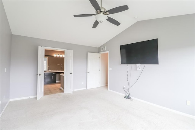 unfurnished bedroom featuring carpet flooring, ensuite bath, lofted ceiling, and ceiling fan