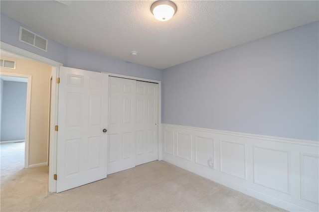 unfurnished bedroom with a closet, a textured ceiling, and light carpet