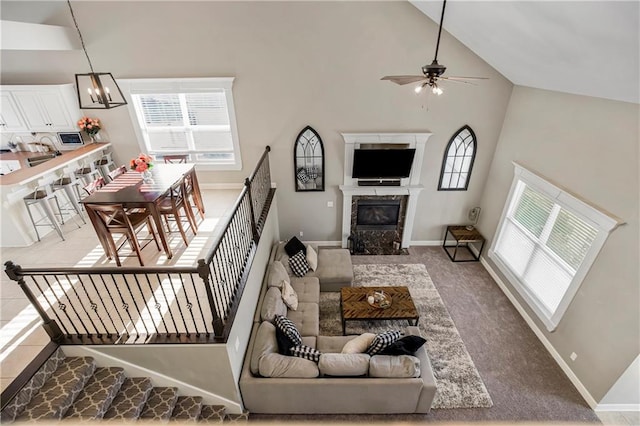 carpeted living room featuring ceiling fan with notable chandelier, a fireplace, high vaulted ceiling, and a healthy amount of sunlight