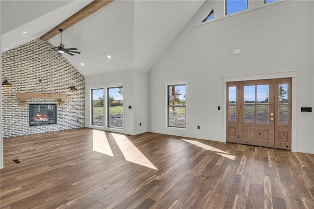 unfurnished living room featuring beam ceiling, ceiling fan, a large fireplace, dark hardwood / wood-style flooring, and high vaulted ceiling