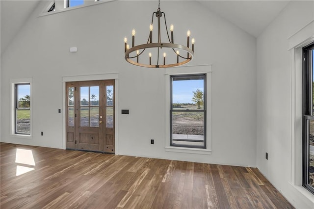 unfurnished dining area with plenty of natural light, high vaulted ceiling, dark wood-type flooring, and an inviting chandelier