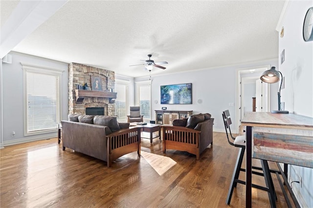 living room featuring ceiling fan, a textured ceiling, dark wood-type flooring, a fireplace, and crown molding