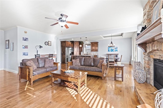 living room with ceiling fan with notable chandelier, light hardwood / wood-style floors, crown molding, and a stone fireplace