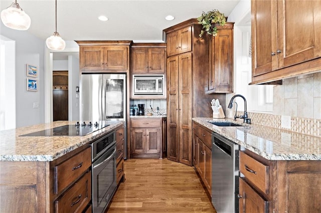 kitchen with light stone counters, hanging light fixtures, sink, stainless steel appliances, and light wood-type flooring