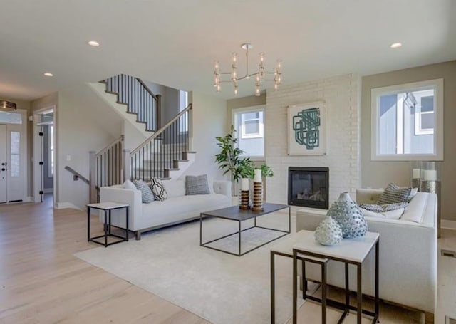 living room with a brick fireplace, light hardwood / wood-style floors, and an inviting chandelier