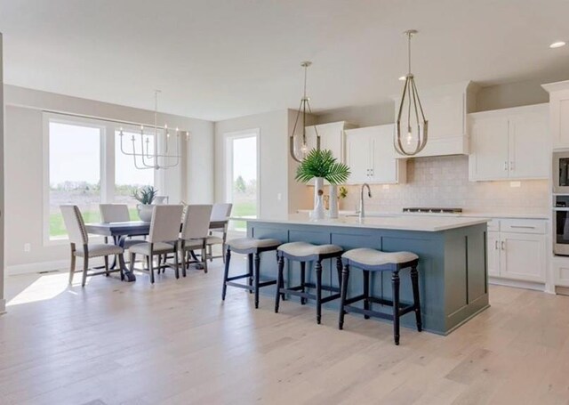 9300 Zarda Dr, Lenexa, KS 66227 - kitchen with an island with sink, decorative backsplash, white cabinets, a sink, and stainless steel oven