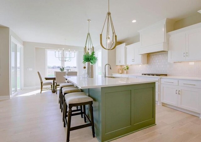 9300 Zarda Dr, Lenexa, KS 66227 - kitchen with tasteful backsplash, light wood-style floors, a sink, white cabinetry, and a center island with sink