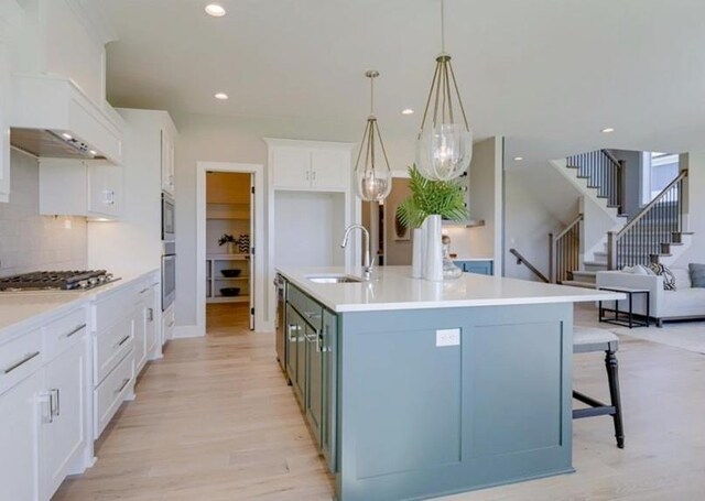 9300 Zarda Dr, Lenexa, KS 66227 - kitchen with a sink, stainless steel appliances, light wood-style floors, a center island with sink, and white cabinetry