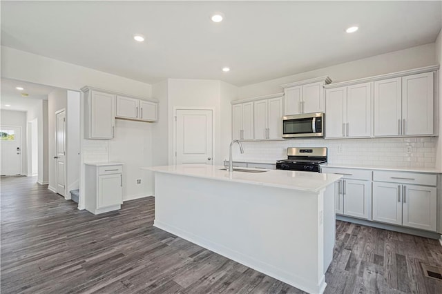 kitchen with decorative backsplash, dark wood-type flooring, sink, appliances with stainless steel finishes, and a center island with sink