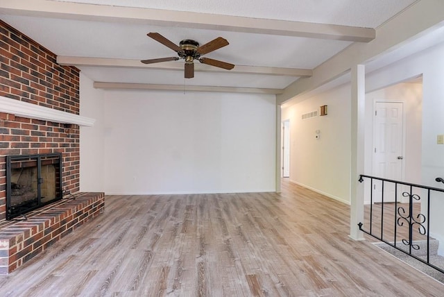 unfurnished living room with a brick fireplace, beam ceiling, light hardwood / wood-style floors, and ceiling fan