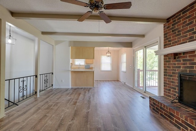 unfurnished living room with light hardwood / wood-style flooring, a textured ceiling, a fireplace, and beamed ceiling