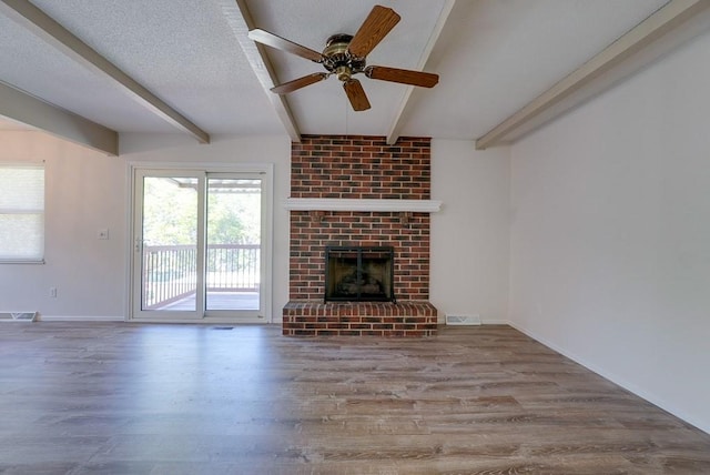 unfurnished living room with ceiling fan, beam ceiling, a brick fireplace, and a textured ceiling