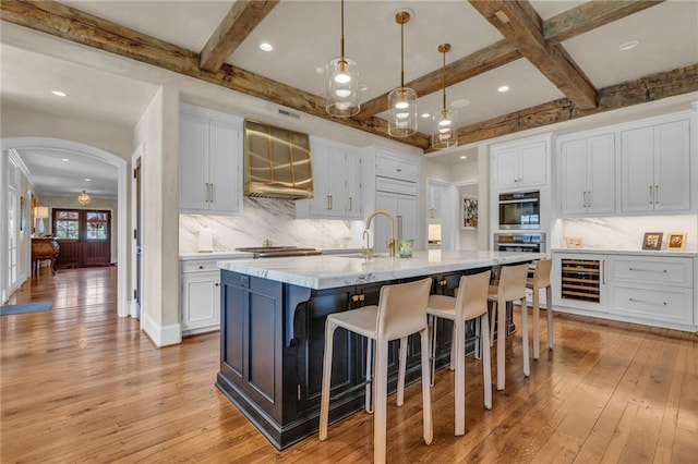 kitchen with light hardwood / wood-style floors, a kitchen island with sink, decorative light fixtures, and white cabinets