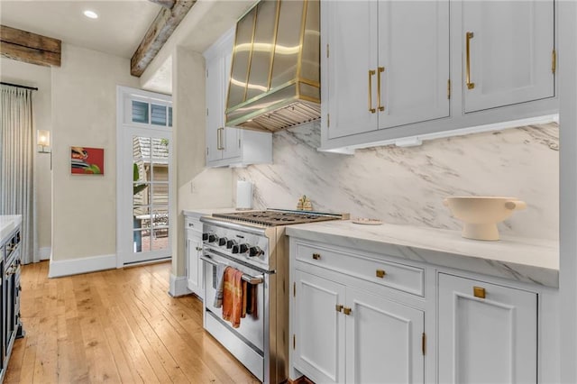 kitchen featuring beam ceiling, custom range hood, stainless steel stove, light wood-type flooring, and white cabinets