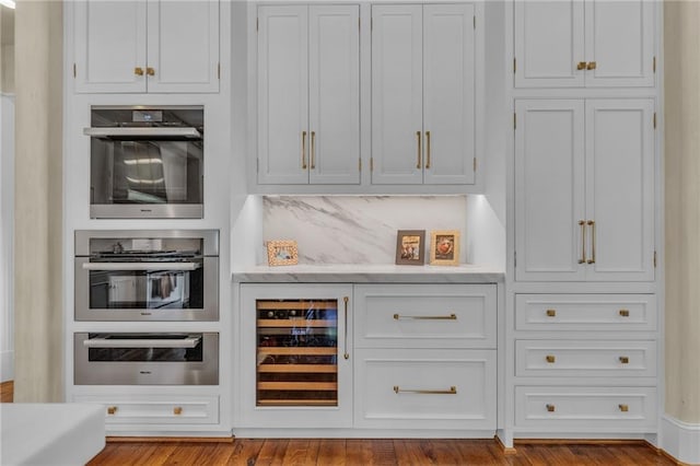 bar with stainless steel double oven, backsplash, beverage cooler, white cabinetry, and light hardwood / wood-style floors