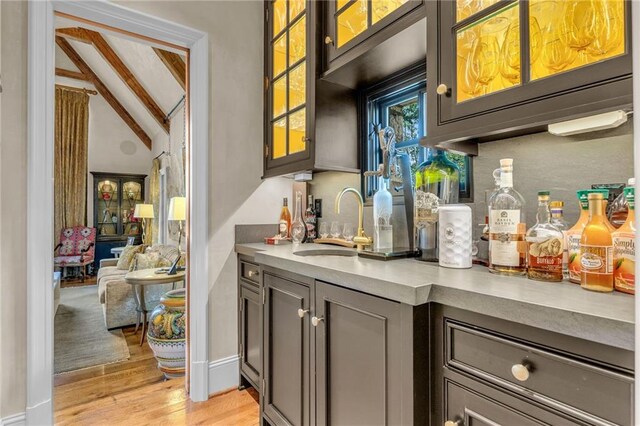 bar featuring sink, lofted ceiling with beams, and light hardwood / wood-style flooring