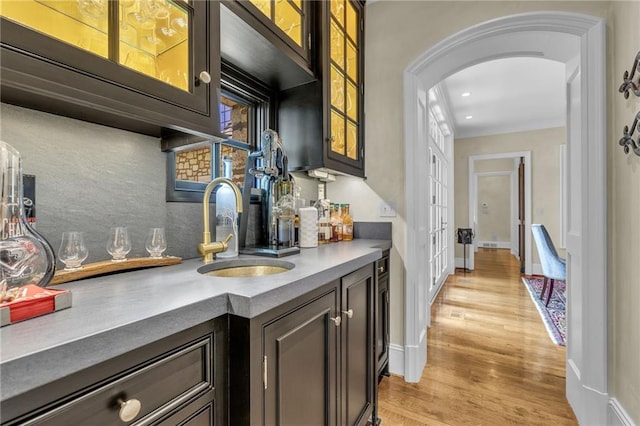 bar with sink, light hardwood / wood-style floors, ornamental molding, and dark brown cabinetry