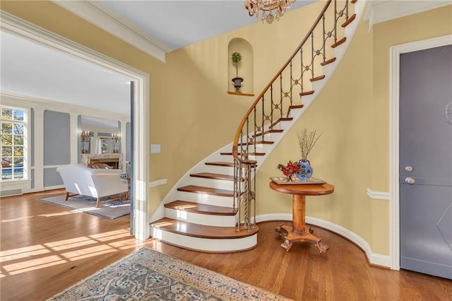 stairs with ornamental molding, hardwood / wood-style floors, and a chandelier