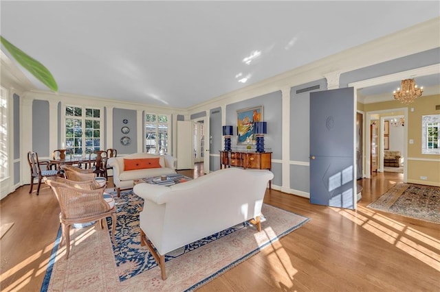 living room featuring an inviting chandelier, light hardwood / wood-style flooring, ornamental molding, and plenty of natural light