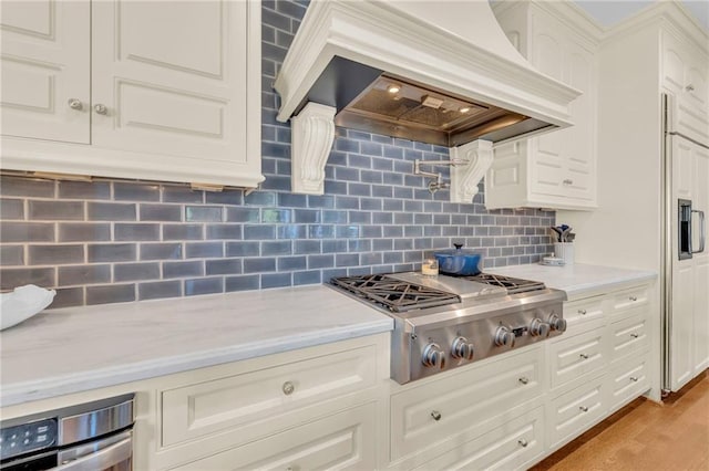 kitchen with backsplash, stainless steel gas cooktop, white cabinetry, custom range hood, and light hardwood / wood-style flooring